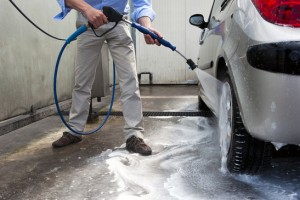 Man, wahsing his car in the stall of a car wash, using a high pressure water jet